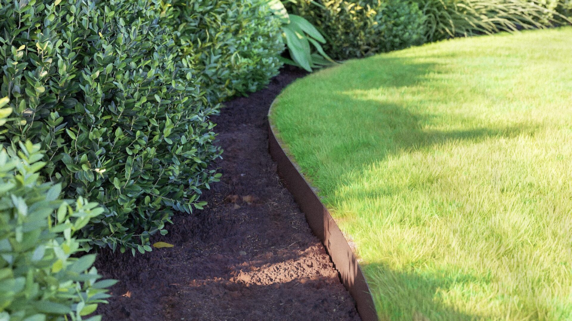 A tidy garden border is formed with CLASSIC flexible steel edging, neatly dividing the green lawn from thick bushes, with a narrow strip of exposed soil between the grass and shrubs.